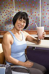 Mature Asian adult female sitting at table in health club cafeteria.