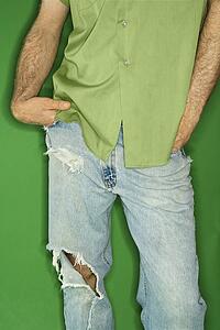 Mid body portrait of Caucasian man in torn blue jeans with hands in pockets.
