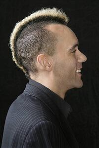 Portrait of Caucasian man in suit with mohawk against black background.