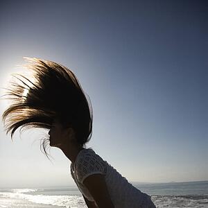 Young Asian female swinging her hair back at the beach with sun in background.
