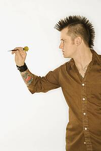 Side view of Caucasian man with mohawk holding and aiming dart against white background.