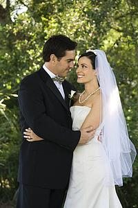 Caucasian mid-adult bride and groom embracing, smiling and looking at each other.