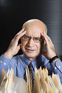 Caucasian middle-aged businessman looking at files with hands on head and grimacing.