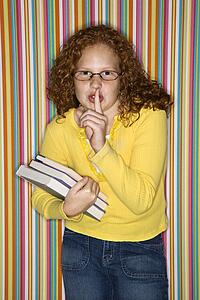 Caucasian female child holding books and holding finger to lips.