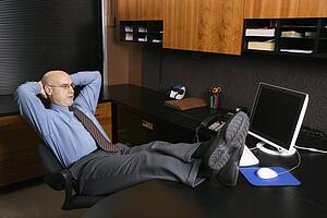 Caucasian middle-aged businessman in office sitting with feet on desk.