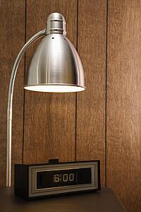 Retro scene of desk lamp shining on retro clock set for 6: 00 against wood paneling.