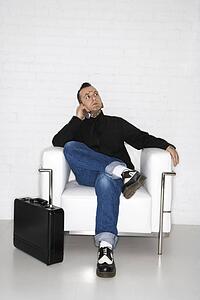 Caucasian mid-adult man with tattoos and piercings talking on cell phone with briefcase.