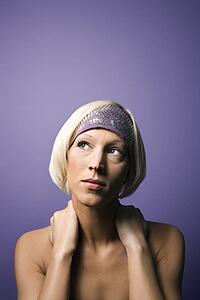 Head and shoulder portrait of bare young adult Caucasian woman on purple background wearing headband.