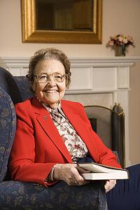 Elderly Caucasian woman reading book in chair at retirement community center.