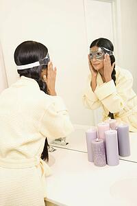 Asian/Indian young woman looking in mirror adjusting eye mask.