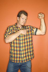Portrait of adult Caucasian man on orange background flexing and showing off his arm muscle.