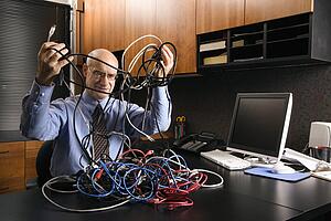 Caucasian middle-aged businessman at desk in office with a tangle of computer cables.