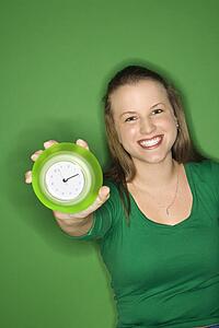 Caucasian young female adult holding out clock and smiling.