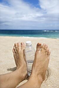 Caucasian young adult woman feet and water bottle on beach.
