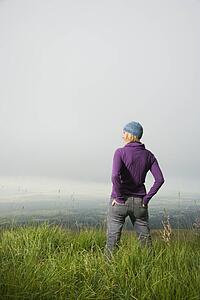 Back view of smiling middle-aged Caucasian woman standing alone in field looking to side.