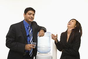 Laughing Vietnamese businesswoman standing at water cooler with Indian businessman.