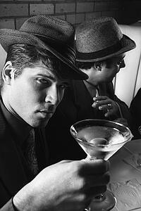 Two Caucasian prime adult males in retro suits sitting at table with cocktails.
