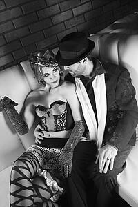 Caucasian prime adult male in retro suit sitting with Caucasian prime adult female in retro wear.
