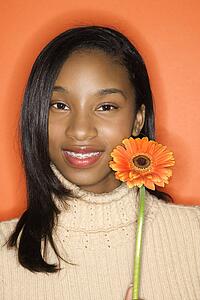 Portrait of smiling African-American teen girl holding single Gerbera Daisy against orange background.