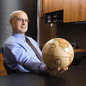 Caucasian middle-aged businessman sitting at desk in office holding globe.