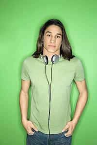 Portrait of Asian-American teen boy with headphones around neck and hands in pockets.