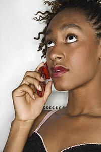 Young sexy African-American woman holding cellphone to ear and rolling eyes upward.