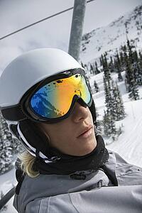 Caucasian teenage boy wearing helmet and goggles riding chair lift at ski resort.