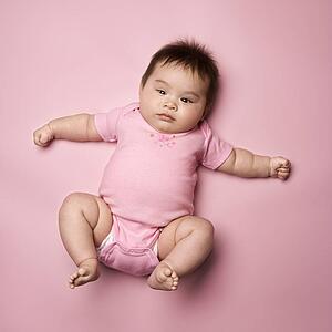 Asian baby lying on back lookin up at viewer with arms out to side.