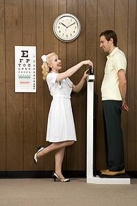 Caucasian mid-adult female nurse weighing man on scale.