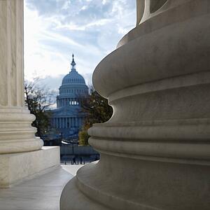 View of Capitol building in distance from behind columns of the Supreme Court building in Washington D. C.