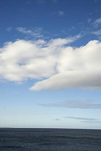 Blue sky with fluffy white clouds over ocean horizen.
