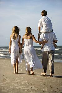 Caucasian family of four walking on beach with dad carrying son on shoulders.
