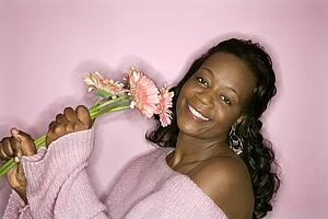 Portrait of smiling African-American mid-adult woman on pink background holding pink flowers.