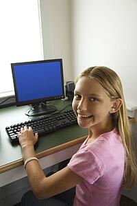 Caucasian pre-teen girl at computer looking over shoulder smiling at viewer.