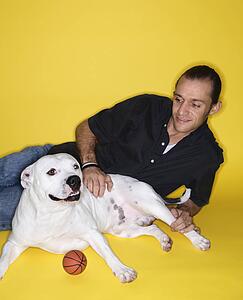 Young adult male Caucasian lying with white Pit Bull dog.
