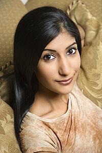 Close up portrait of Asian/Indian young woman sitting on couch.