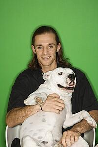 Caucasian mid-adult man holding white Pit Bull on lap.