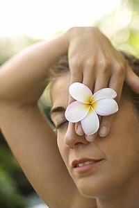 Caucasian mid-adult woman holding plumeria flower over eye.