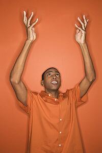 Young African-American man throwing his arms up in the air wearing orange clothing on orange background.