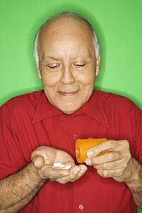 Mature adult Caucasian male emptying pill bottle into hand.