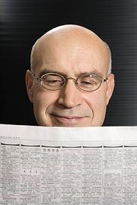 Head shot of Caucasian middle-aged businessman reading newspaper.