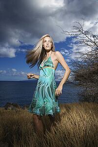 Caucasian young adult blond woman standing in field on coast with hair swinging out.
