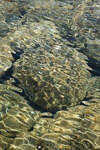 Rocks seen through clear, rippled water with dappled sunlight in Maui, Hawaii.