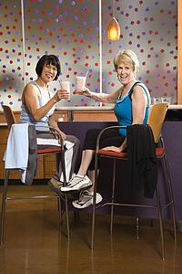 Mature Asian and Caucasian adult females sitting at table in health club cafeteria.