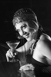 Caucasian prime adult retro female sitting at bar with martini looking at viewer.