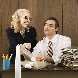 Mid-adult Caucasian male holding printout from calculator as Caucasian female points. 