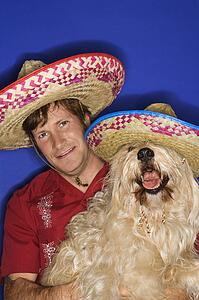 Fluffy brown dog and Caucasian male young adult wearing Mexican sombreros.