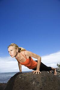Caucasian young adult woman doing push up on rock.