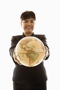 Filipino middle-aged businesswoman holding globe in both hands standing in front of white background.