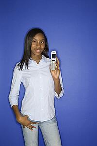 Portrait of African-American teen girl holding cellphone and hand in pocket standing against blue background.
